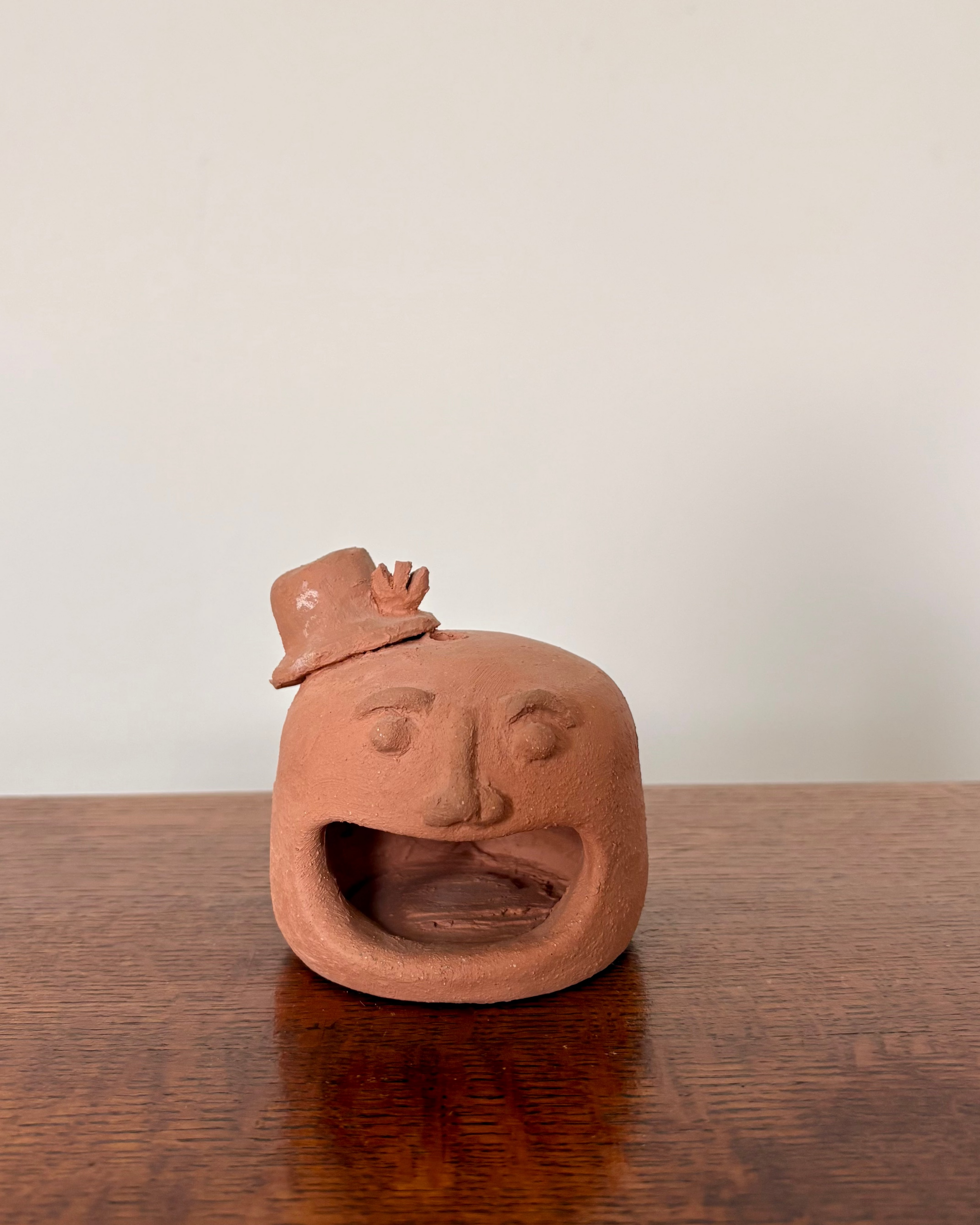 Ceramic sculpture of a face with a hat on a wooden table